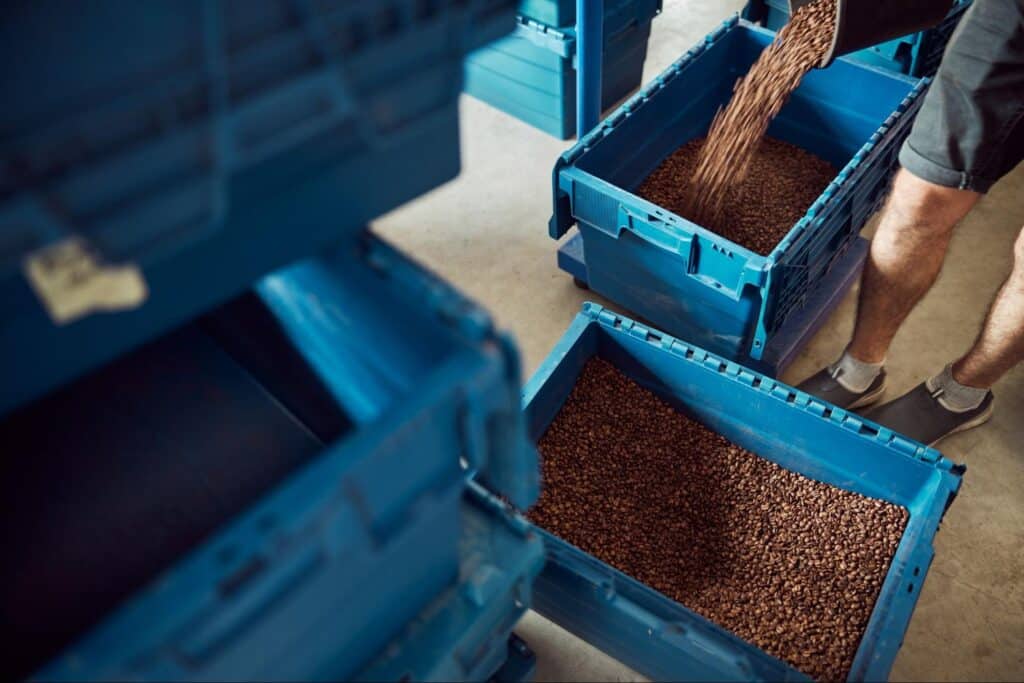 Pouring fresh coffee beans into blue storage bins for optimal storage and organization.