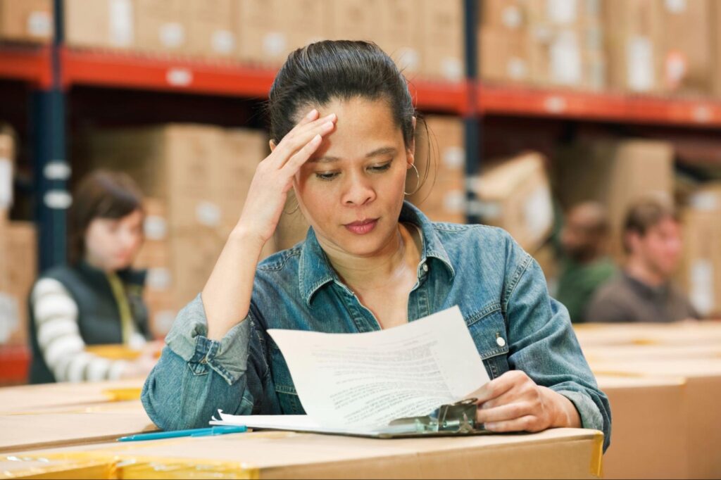 Warehouse worker reviewing paperwork while managing inventory challenges.