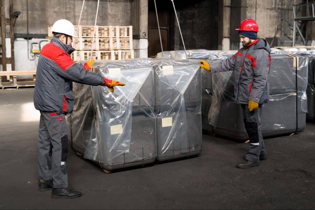 Workers handling large industrial packages in a warehouse setting.