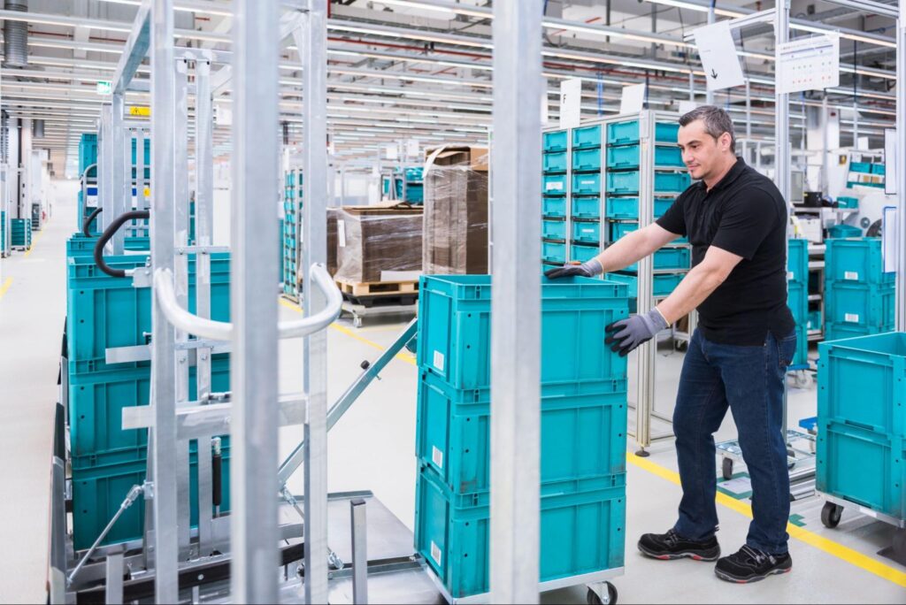 Warehouse worker efficiently moving storage containers in a bustling distribution center.