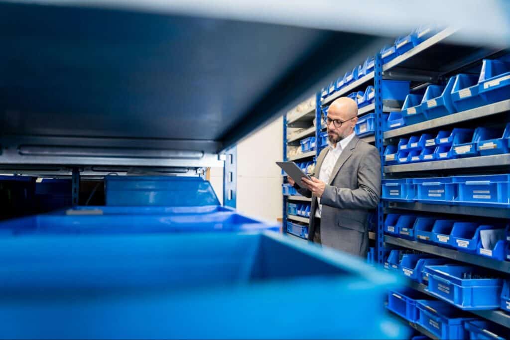 C-suite professional analyzes inventory in a warehouse with blue storage bins.