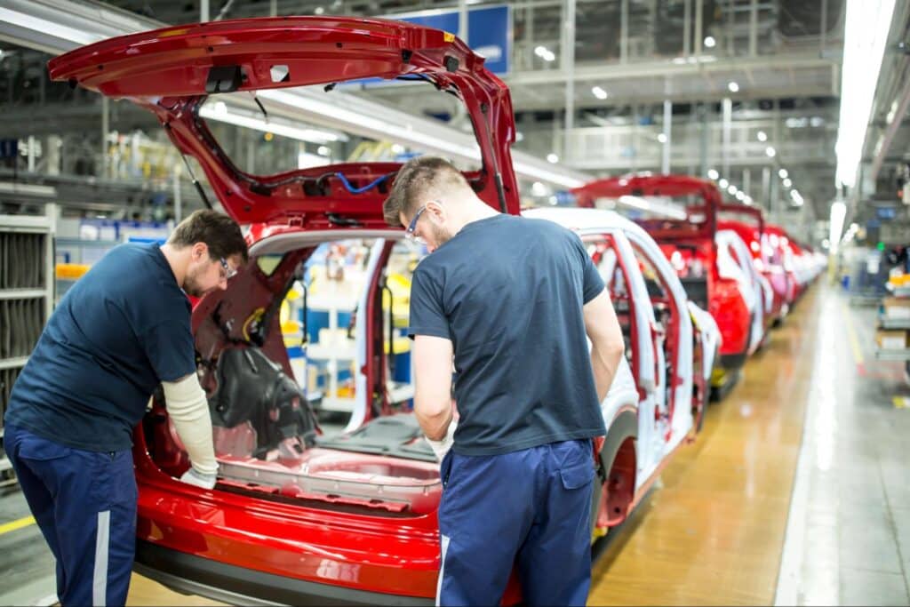 Workers assembling red cars on a factory line, showcasing automotive manufacturing efficiency.